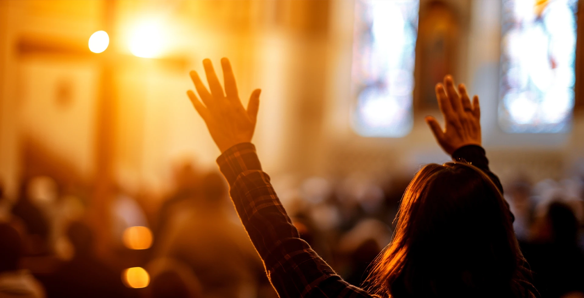 A worshipper raising their hands in a warmly lit service